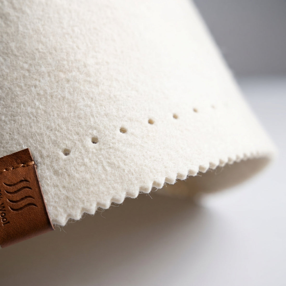 Macro of cream merino wool felt showing its thickness, punched dots and zigzag pinked edge