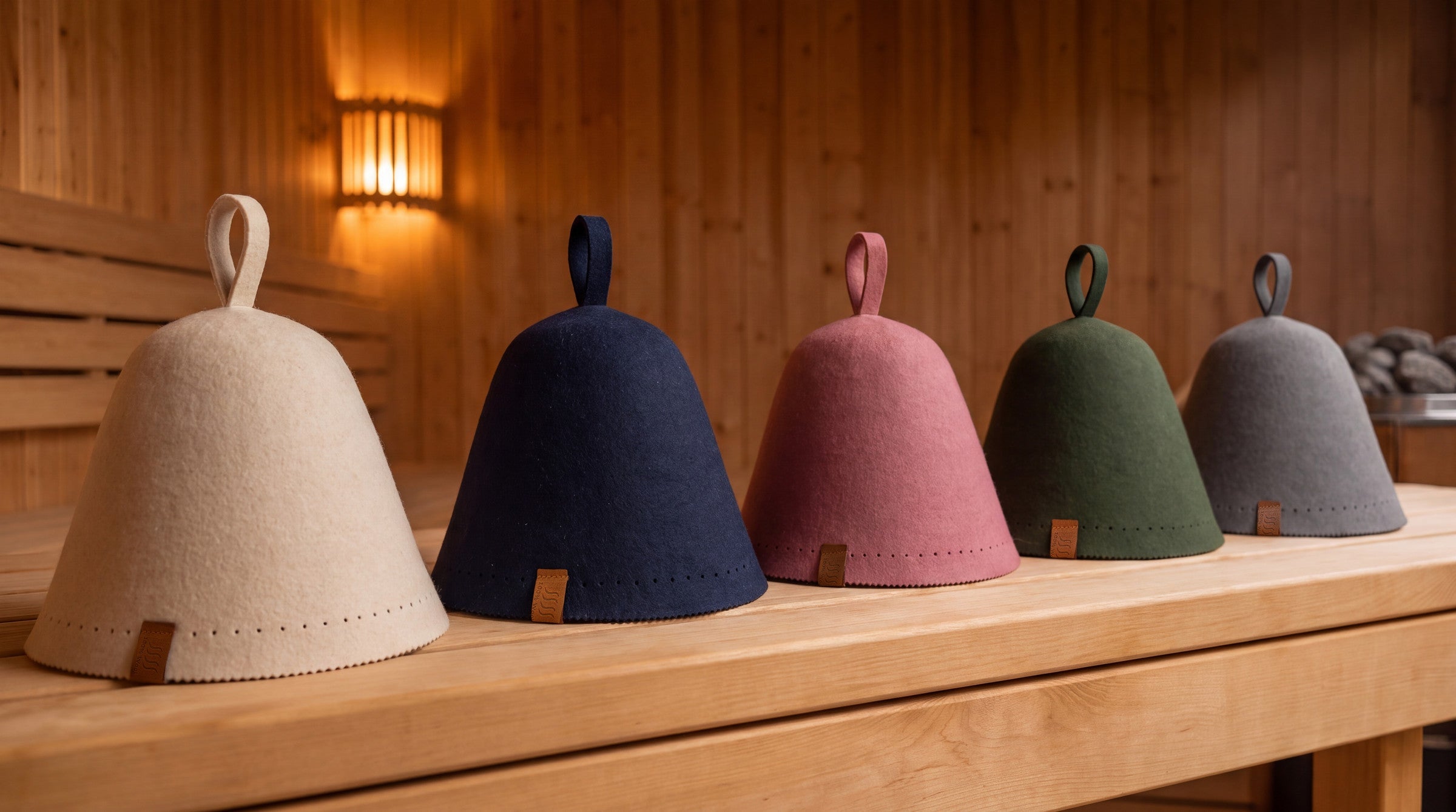 Five Saunatar merino wool sauna hats lined up on a cedar bench in a warmly lit sauna